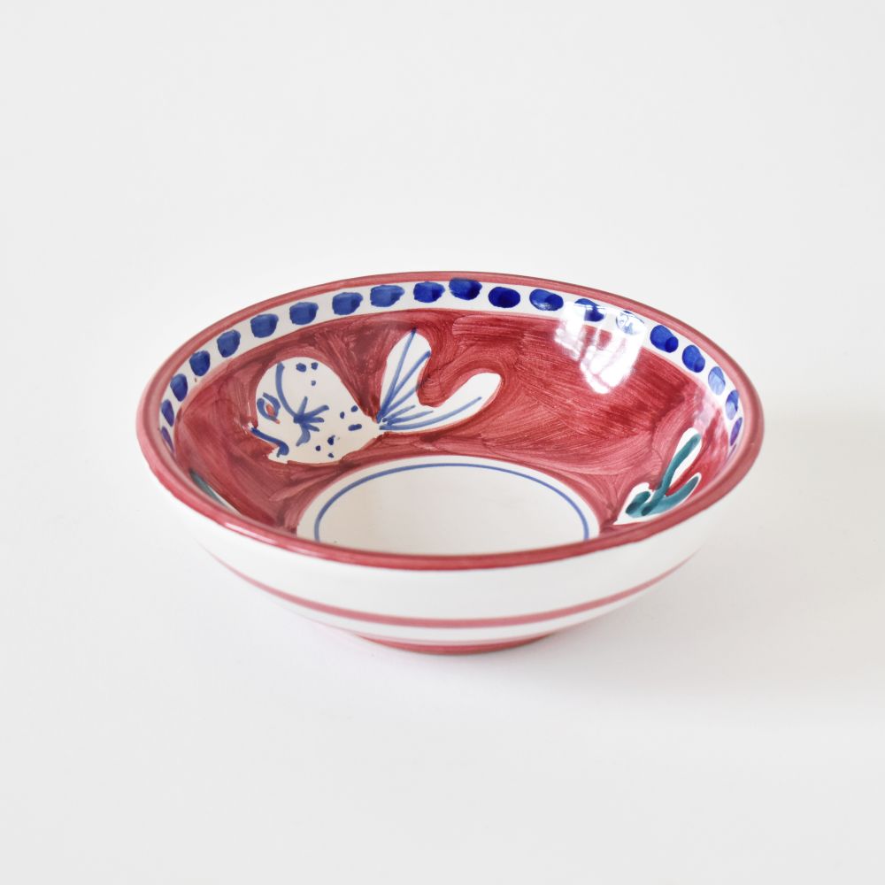 A small bowl with white and deep blue fish painted on a red background. The bowl is displayed on a white background. 