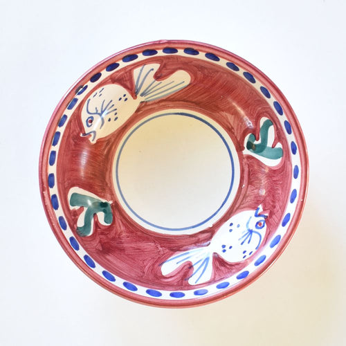 A small bowl with white and deep blue fish painted on a red background. The bowl is displayed on a white background. 